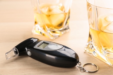Photo of Modern breathalyzer and alcohol on wooden table
