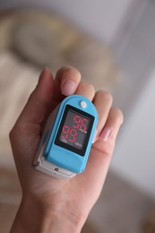 Woman measuring oxygen level with modern fingertip pulse oximeter indoors, closeup