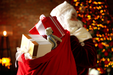 Photo of Santa Claus holding bag full of Christmas gifts against blurred festive lights