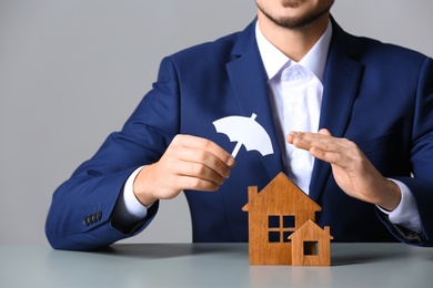 Man covering wooden houses with umbrella cutout at table, closeup. Home insurance