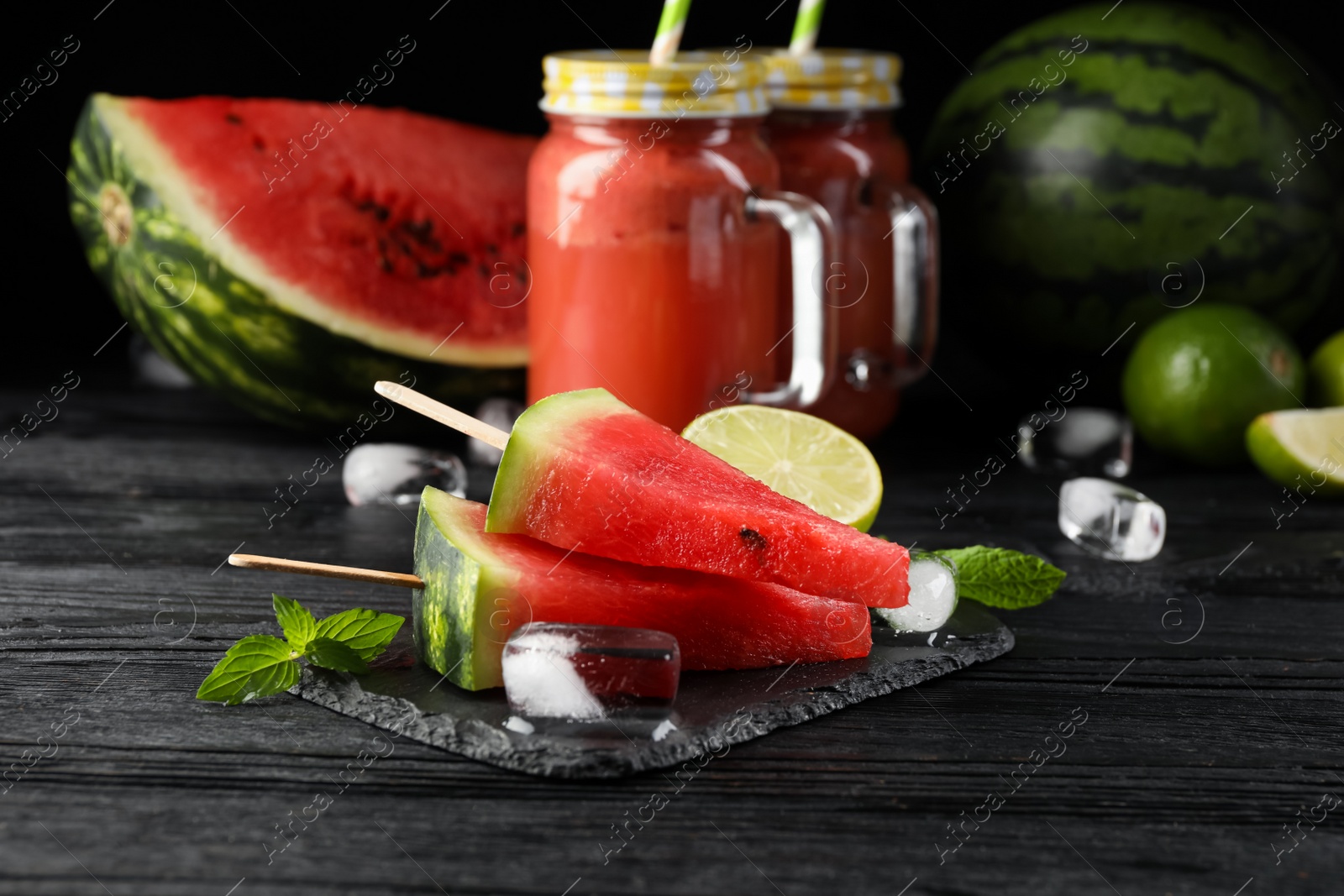 Photo of Slate board with juicy watermelon, ice and lime on black wooden table