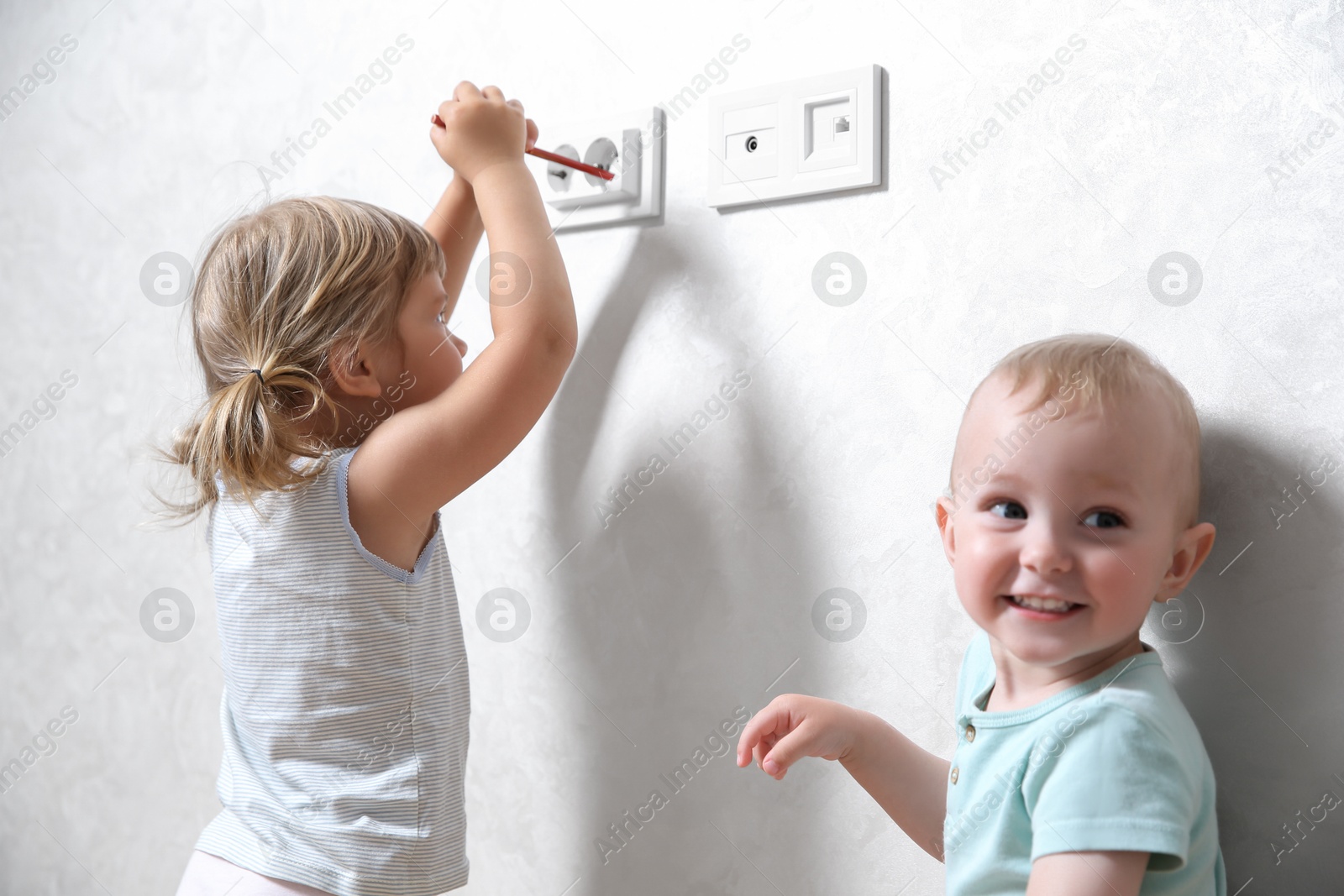 Photo of Little children playing with electrical socket indoors. Dangerous situation