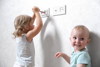 Photo of Little children playing with electrical socket indoors. Dangerous situation