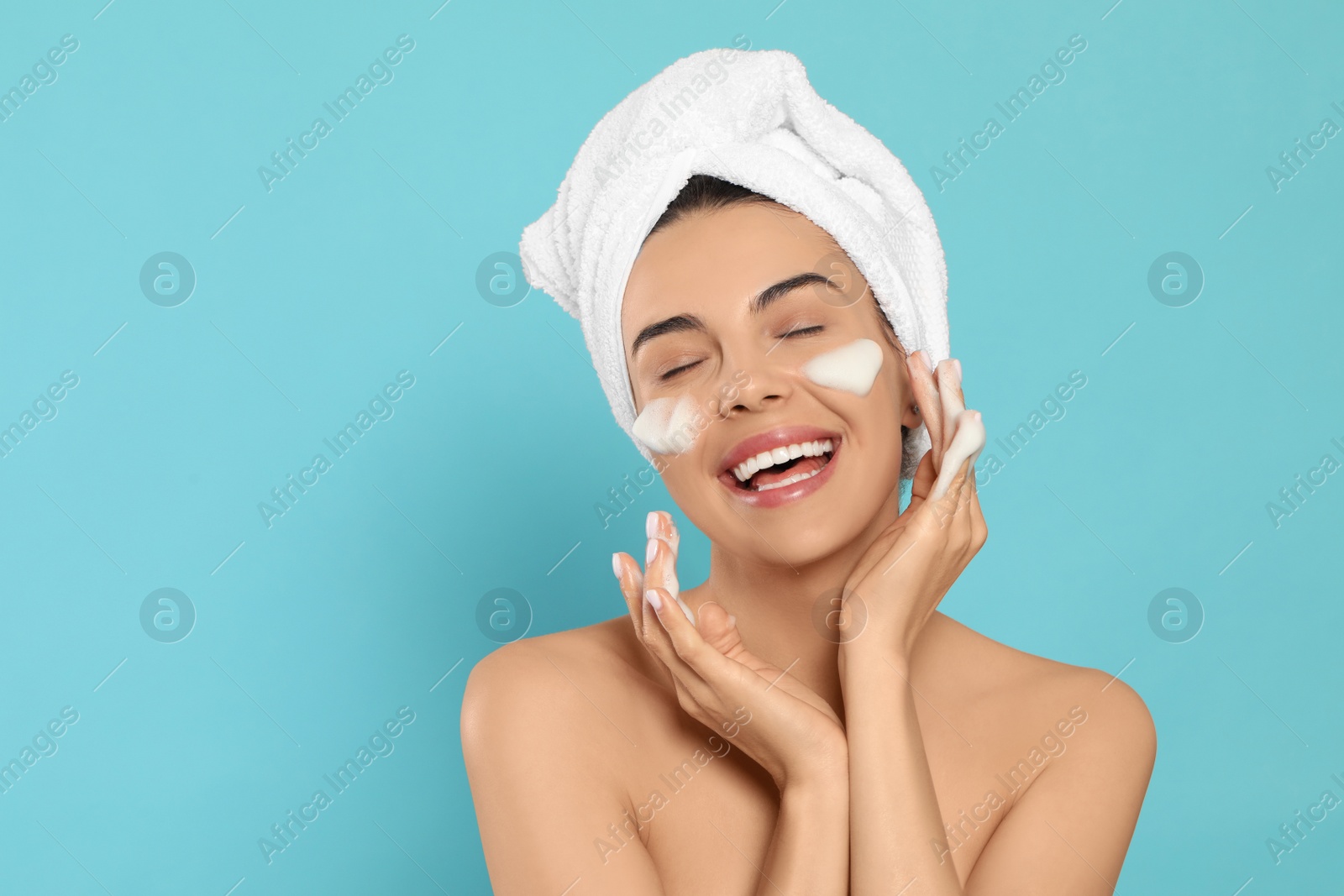 Photo of Happy young woman washing face with cosmetic product on light blue background, space for text