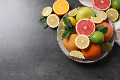 Photo of Different fresh citrus fruits and leaves on grey textured table, flat lay. Space for text