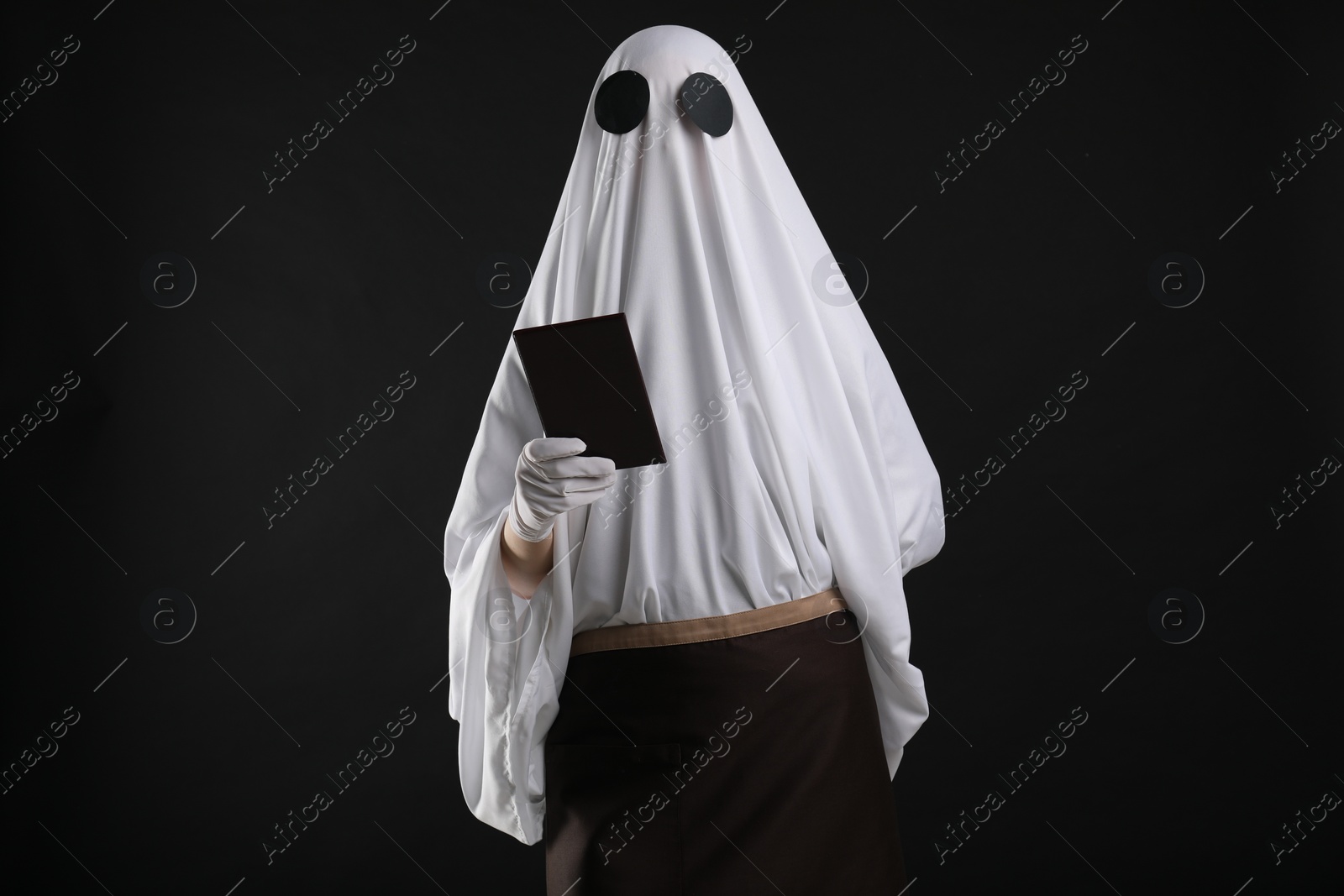 Photo of Creepy ghost. Waiter in white sheet and apron with receipt on black background