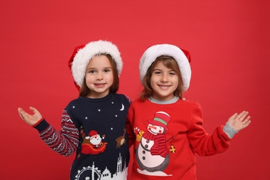 Photo of Kids in Christmas sweaters and Santa hats on red background