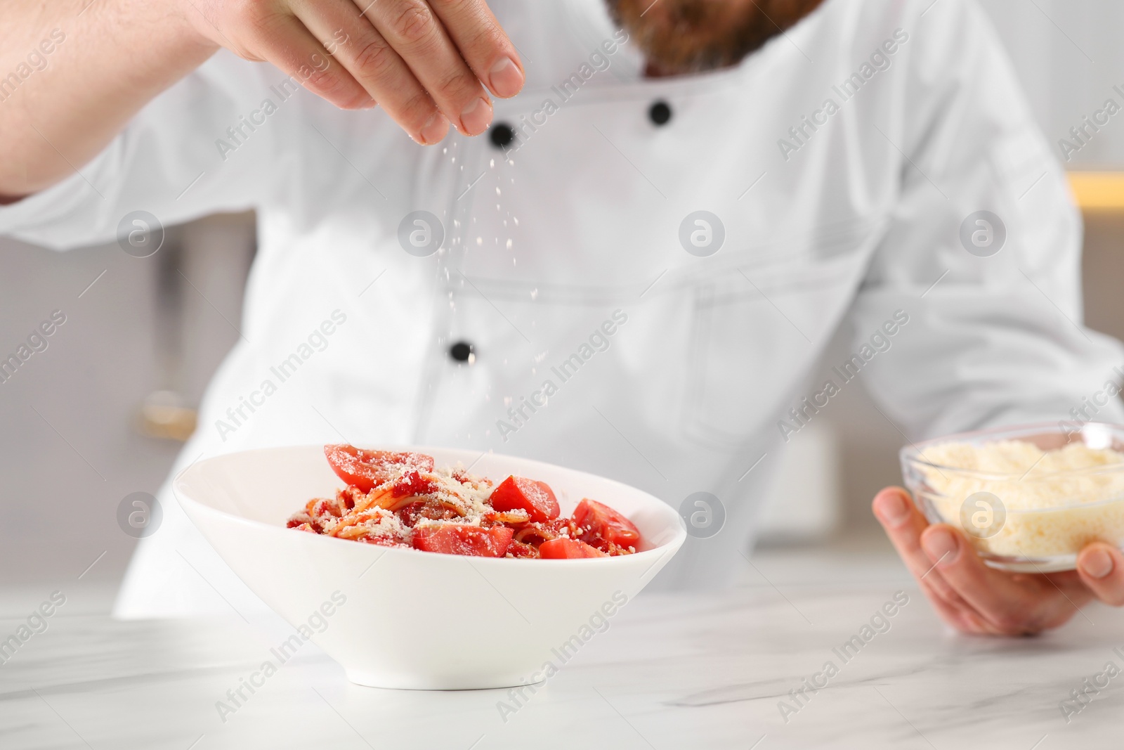 Photo of Closeup of professional chef adding grated cheese into delicious spaghetti at marble table, focus on food