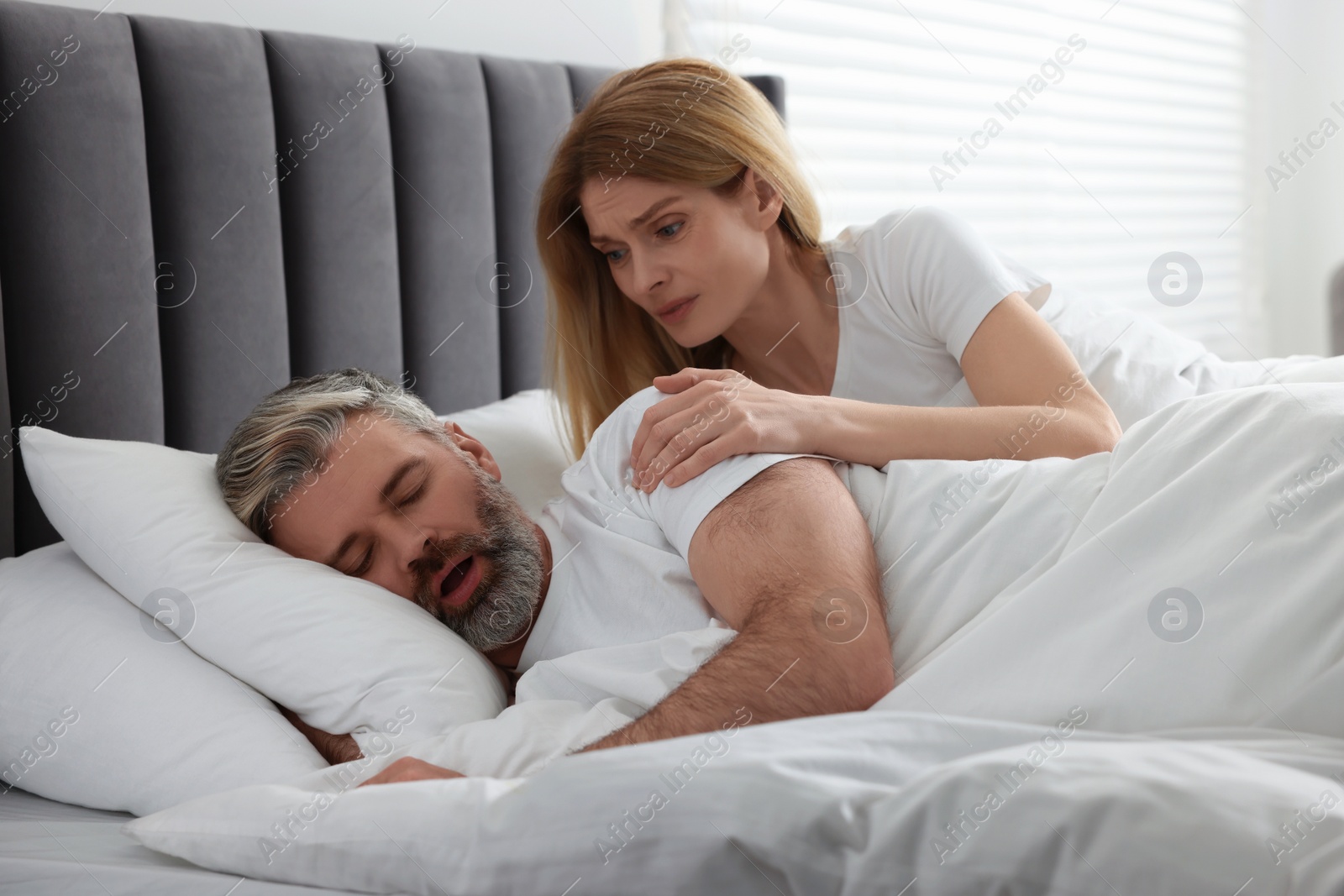 Photo of Irritated woman waking up her snoring husband in bed at home