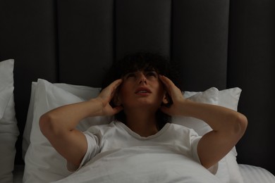 Photo of Young woman suffering from headache in bed at night