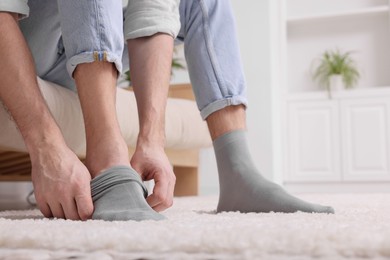 Photo of Man putting on grey socks at home, closeup