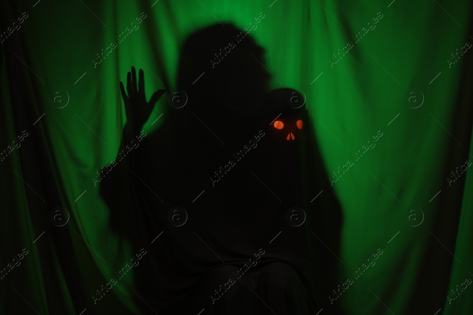 Photo of Silhouette of creepy ghost with skull behind dark green cloth