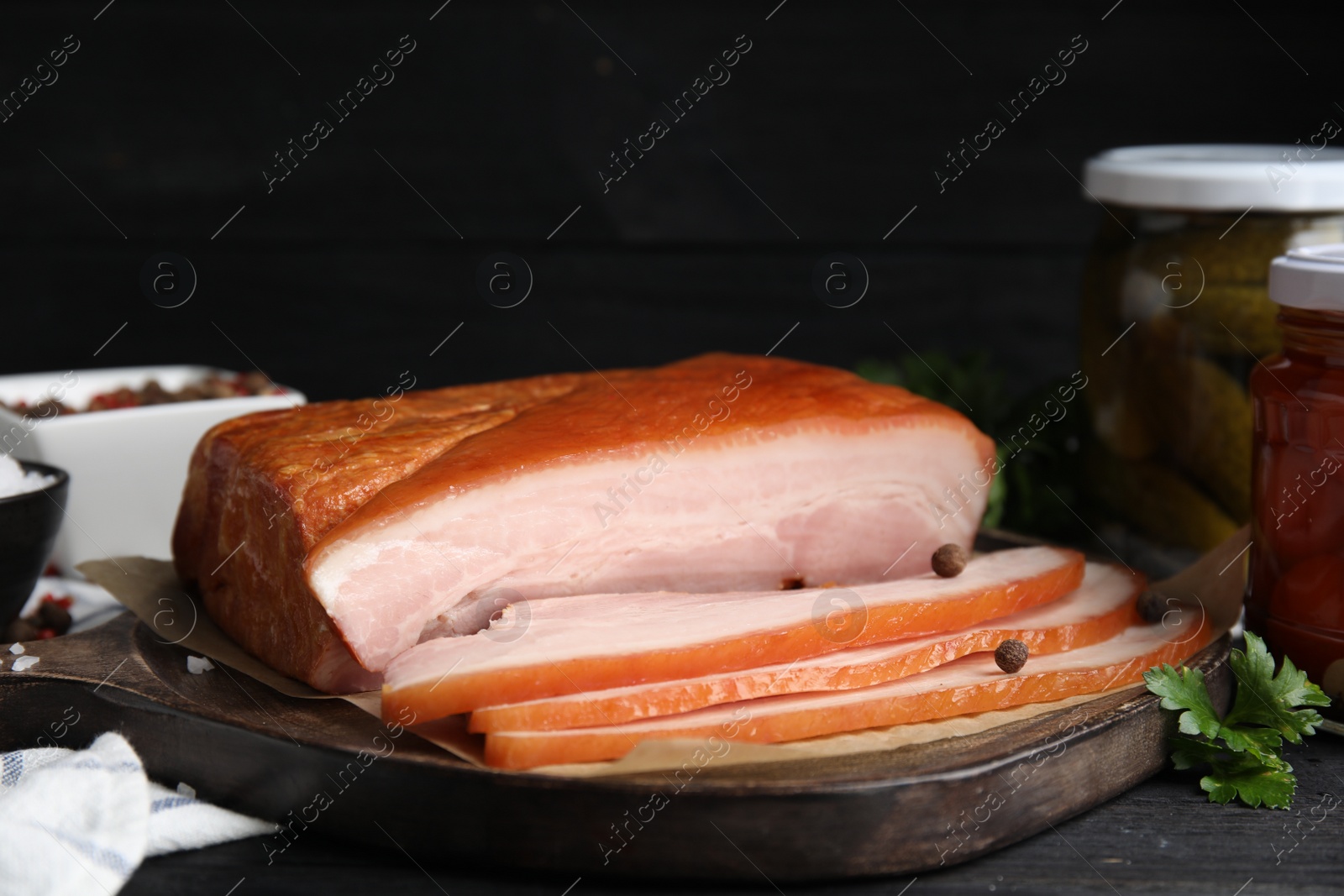 Photo of Delicious smoked bacon with spices and parsley on black table, closeup