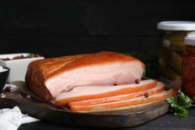 Photo of Delicious smoked bacon with spices and parsley on black table, closeup