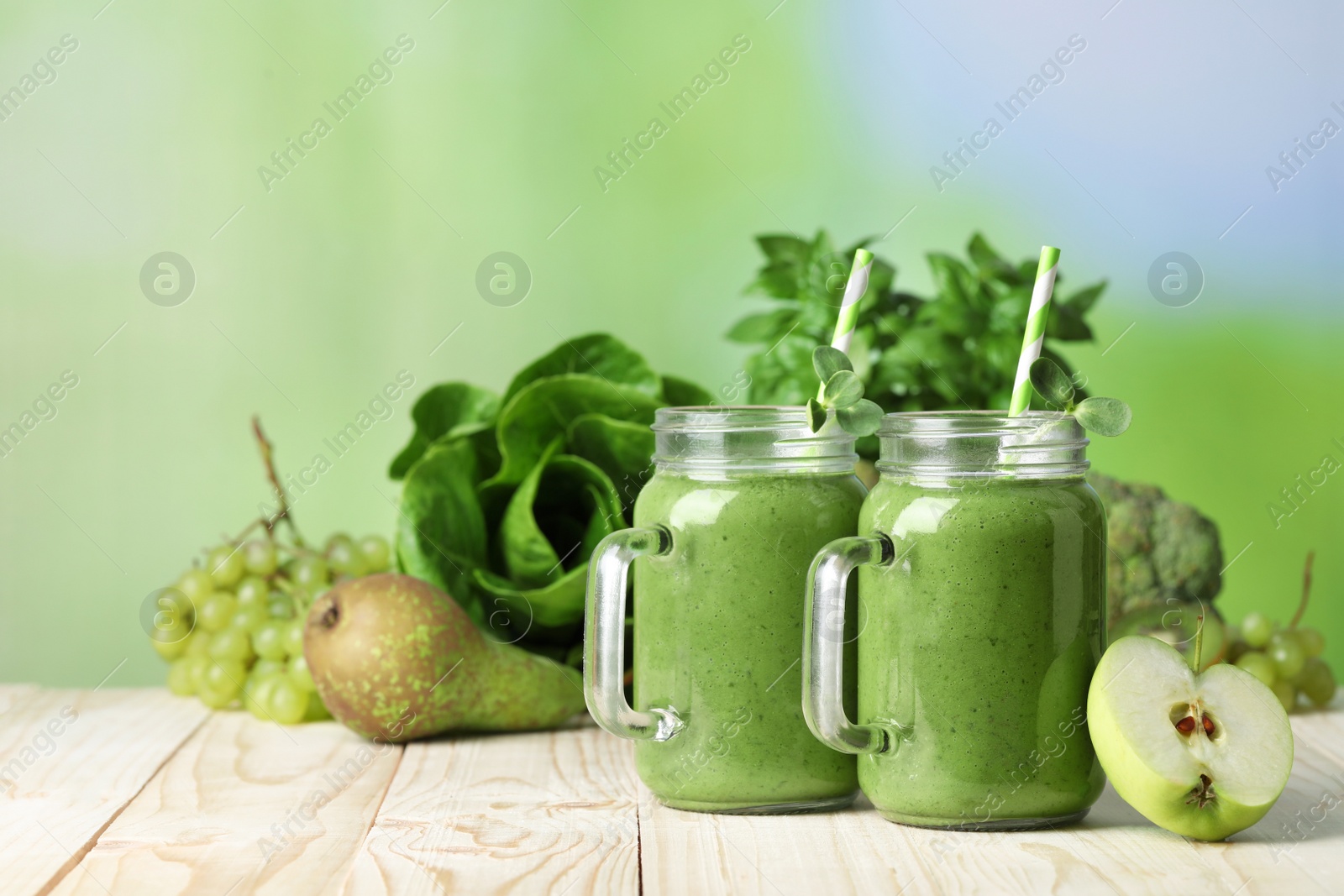 Photo of Mason jars of fresh green smoothie and ingredients on wooden table. Space for text