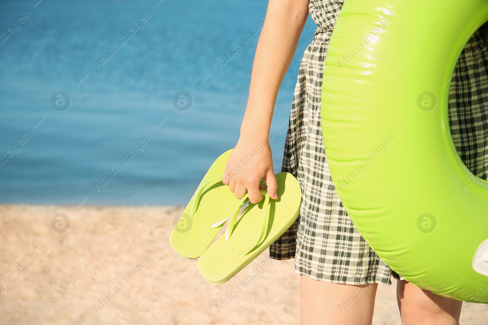 Photo of Woman holding inflatable ring and flip-flops on beach, closeup. Space for text