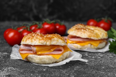 Photo of Delicious bagels with ham and cheese on dark grey textured table, space for text