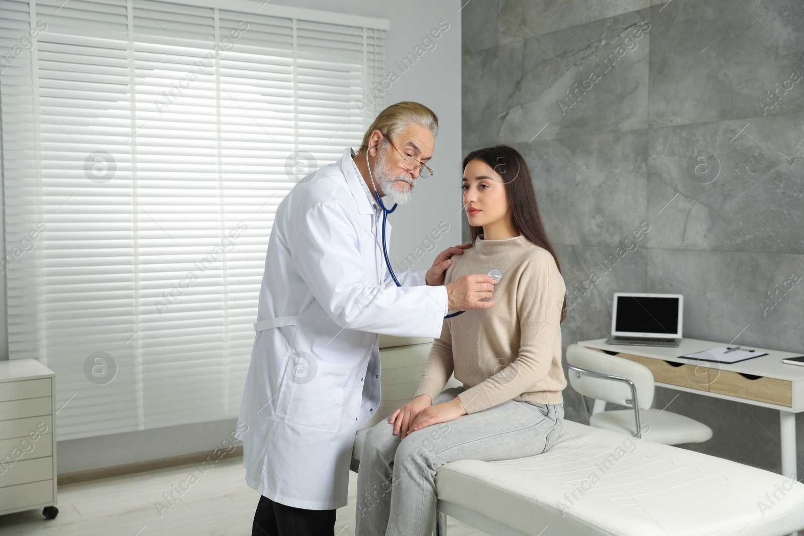 Photo of Senior doctor examining patient with stethoscope in clinic