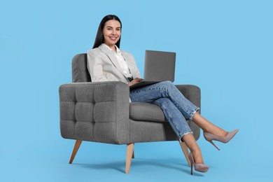 Photo of Happy woman with laptop sitting in armchair on light blue background