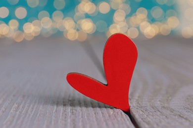 Red decorative heart on grey wooden table against blurred lights, closeup