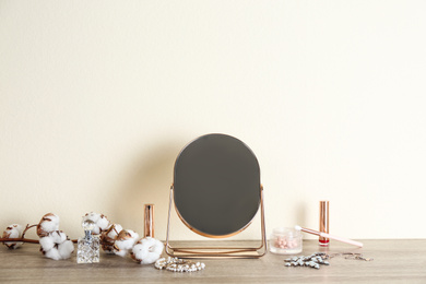 Mirror, makeup products and jewelry on wooden table near light wall