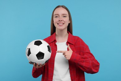 Happy sports fan with ball on light blue background