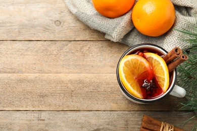 Mug with aromatic mulled wine and oranges on wooden table, flat lay. Space for text