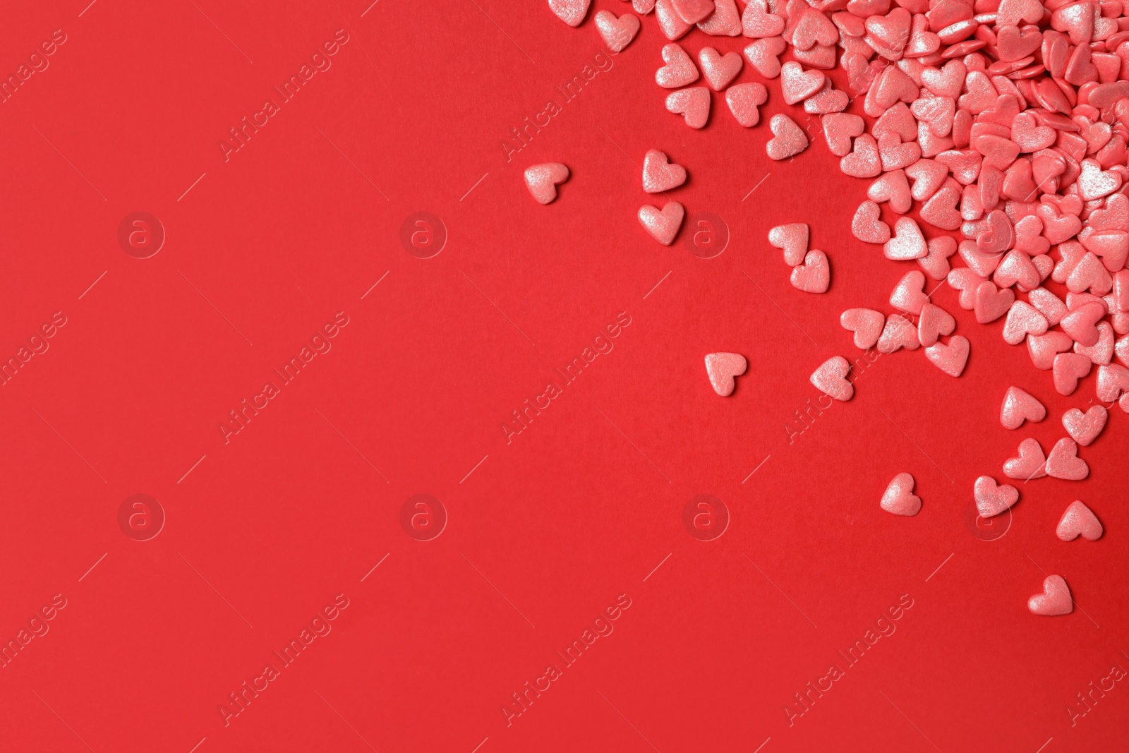 Photo of Bright heart shaped sprinkles on red background, flat lay. Space for text