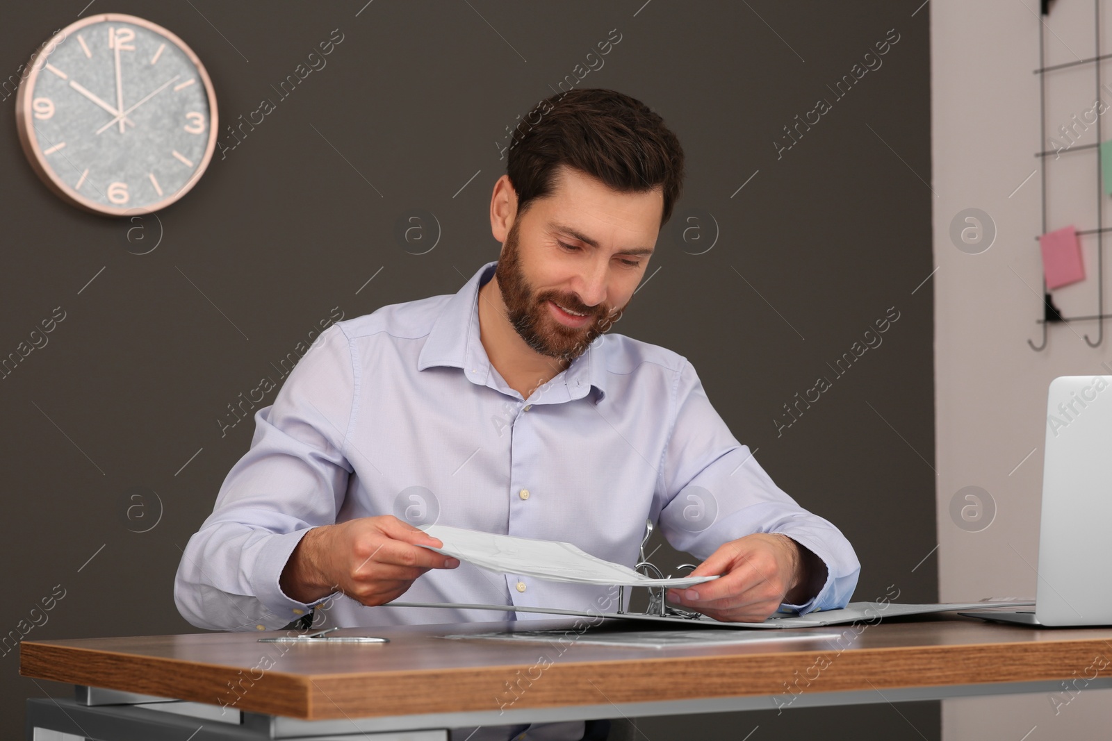 Photo of Businessman putting document into file folder at wooden table in office