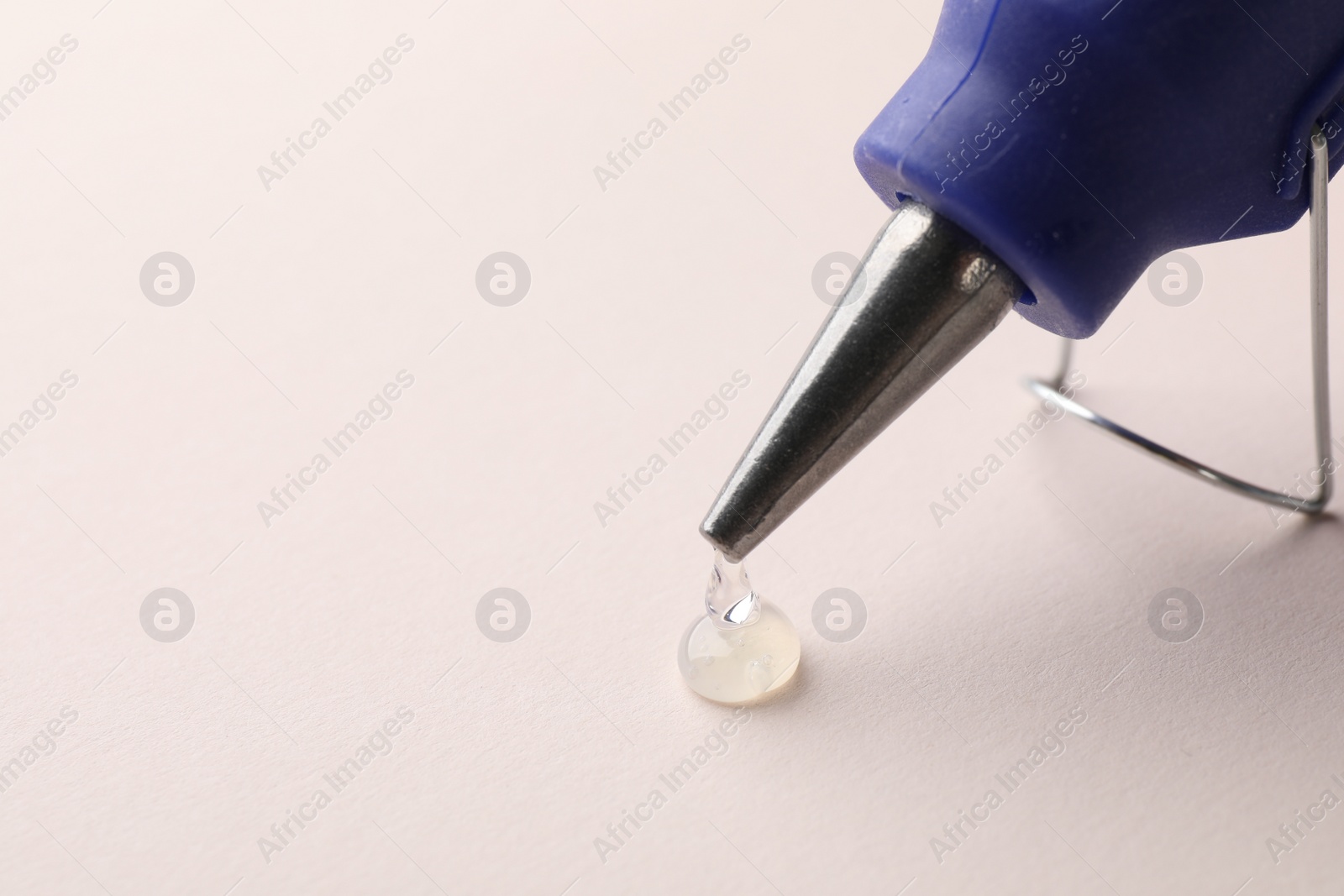 Photo of Melted glue dripping from hot gun on white table, closeup. Space for text