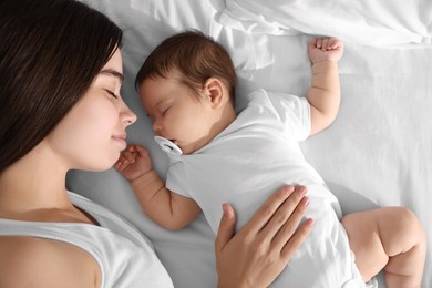 Young mother resting near her sleeping baby on bed, top view