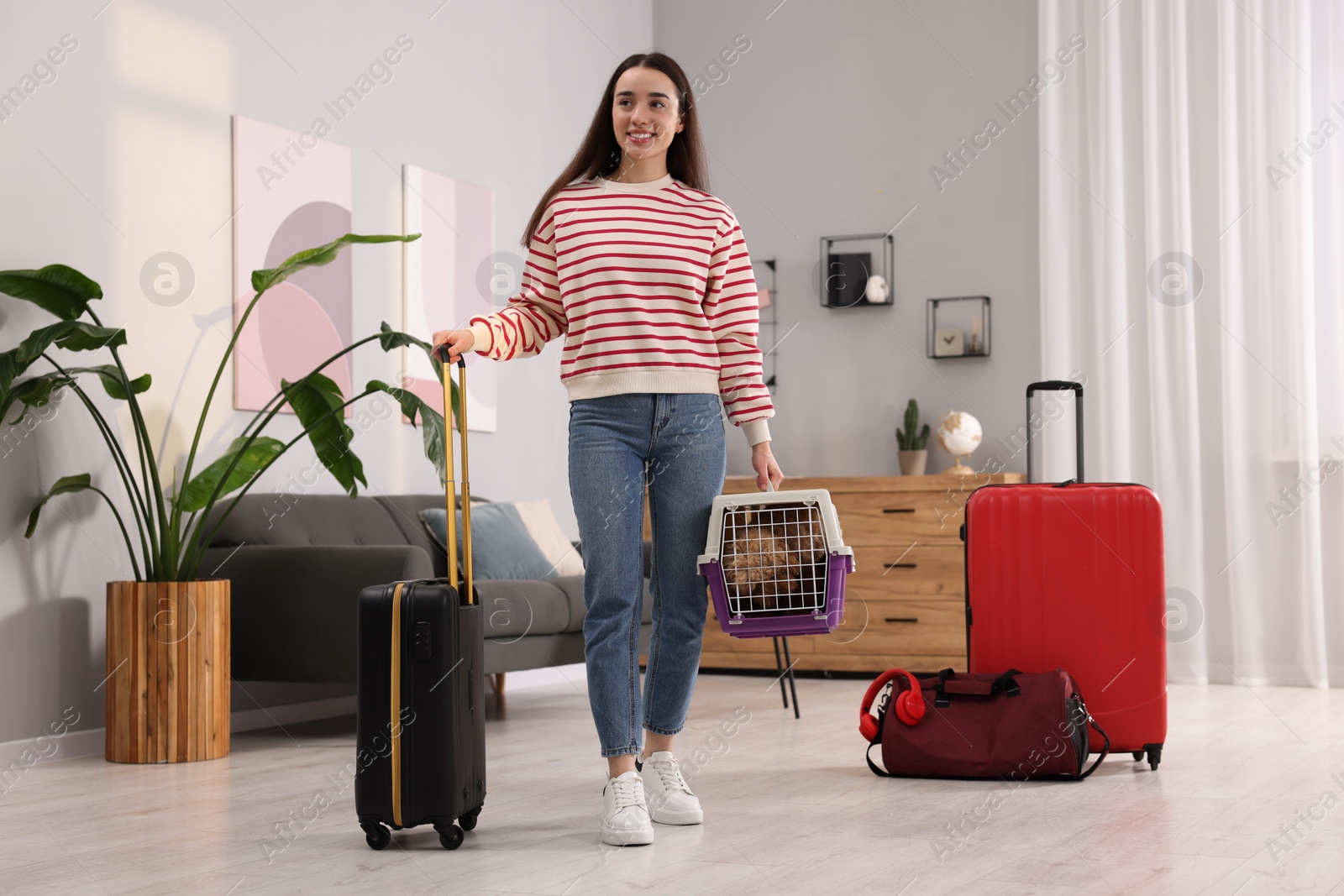 Photo of Travel with pet. Smiling woman holding carrier with dog and suitcase at home