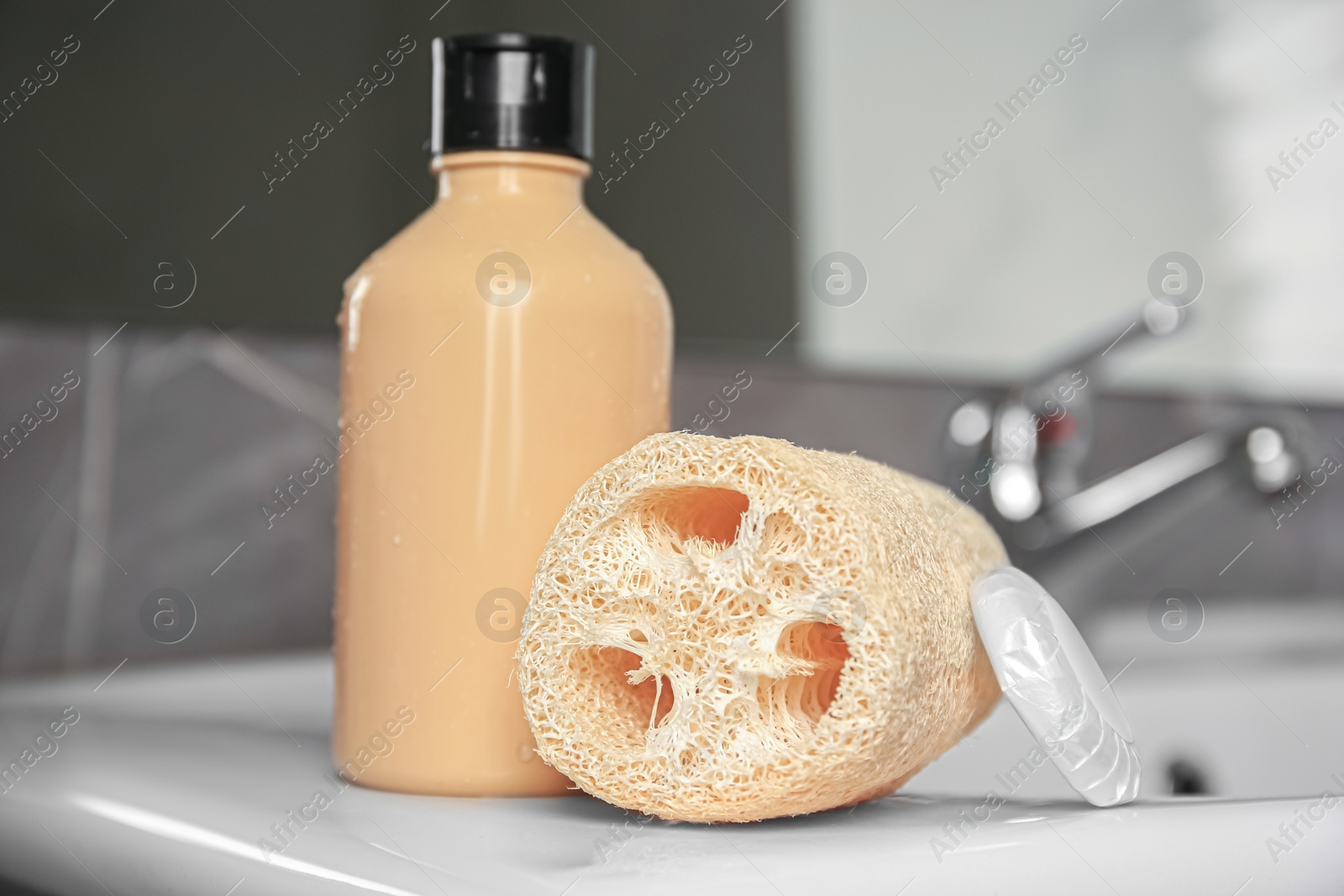 Photo of Natural loofah sponge and shower gel bottle on washbasin in bathroom, closeup