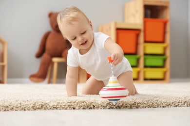 Children toys. Cute little boy playing with spinning top on rug at home