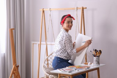 Happy woman artist drawing picture on canvas in studio