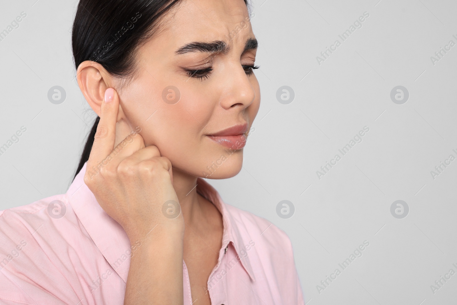 Photo of Young woman suffering from ear pain on light grey background, closeup