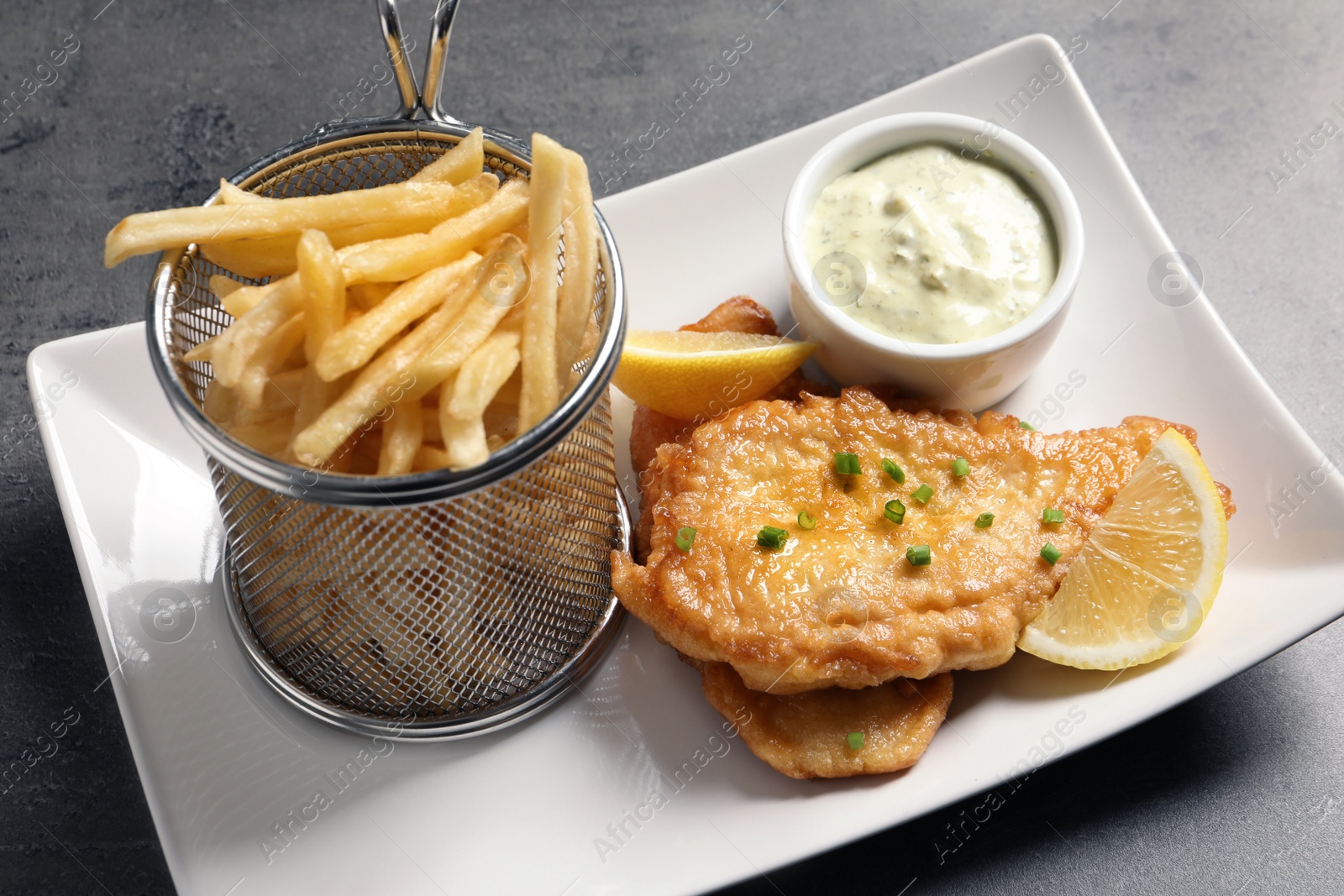 Photo of Plate with British traditional fish and potato chips on grey table