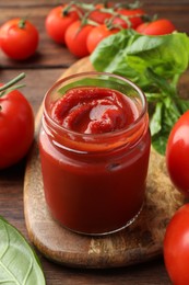 Jar of tasty ketchup and tomatoes on wooden table, closeup
