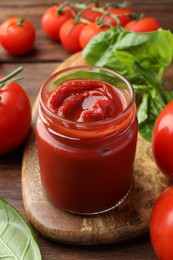 Photo of Jar of tasty ketchup and tomatoes on wooden table, closeup