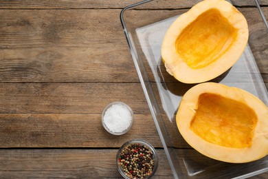 Raw spaghetti squash halves in glass baking dish and spices on wooden table, flat lay. Space for text