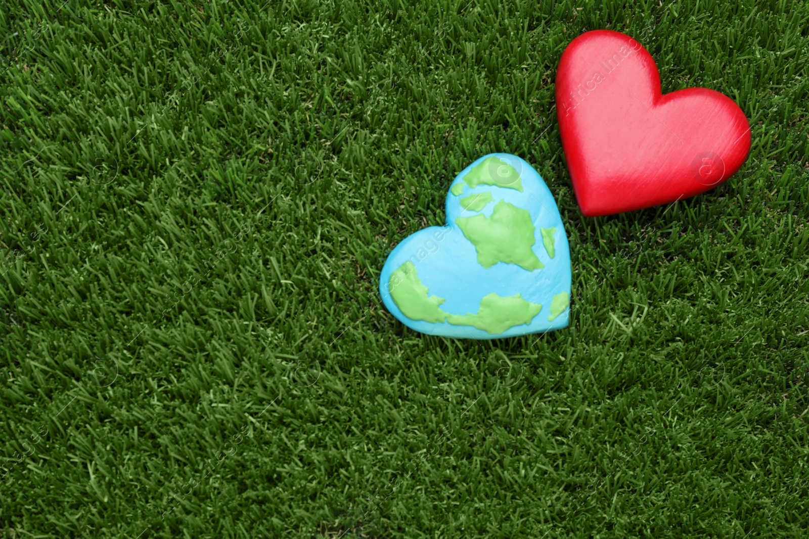 Photo of Happy Earth Day. Plasticine planet and decorative heart on green grass, flat lay with space for text