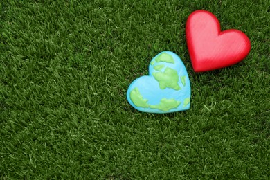 Photo of Happy Earth Day. Plasticine planet and decorative heart on green grass, flat lay with space for text