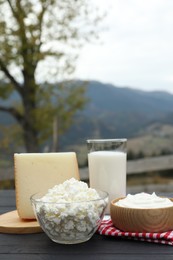 Photo of Tasty cottage cheese and other fresh dairy products on black wooden table in mountains