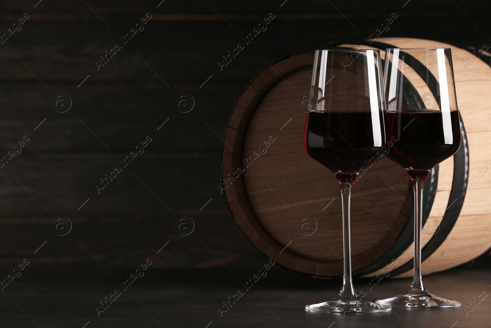 Photo of Glasses of red wine and wooden barrel on table against dark background. Space for text