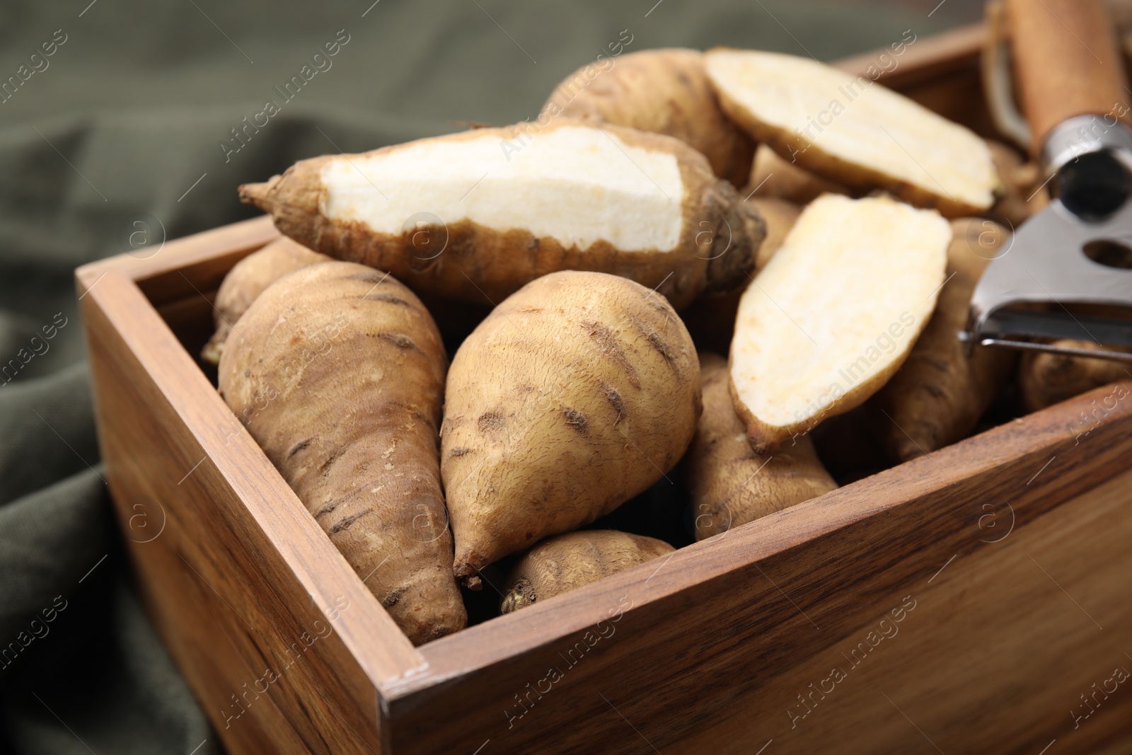 Photo of Tubers of turnip rooted chervil and peeler in wooden crate on table, closeup