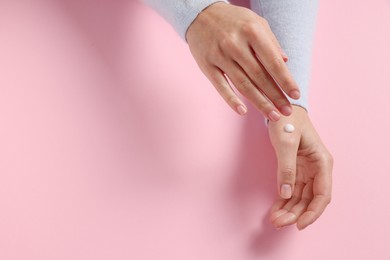 Woman applying cosmetic cream onto hand on pink background, top view. Space for text