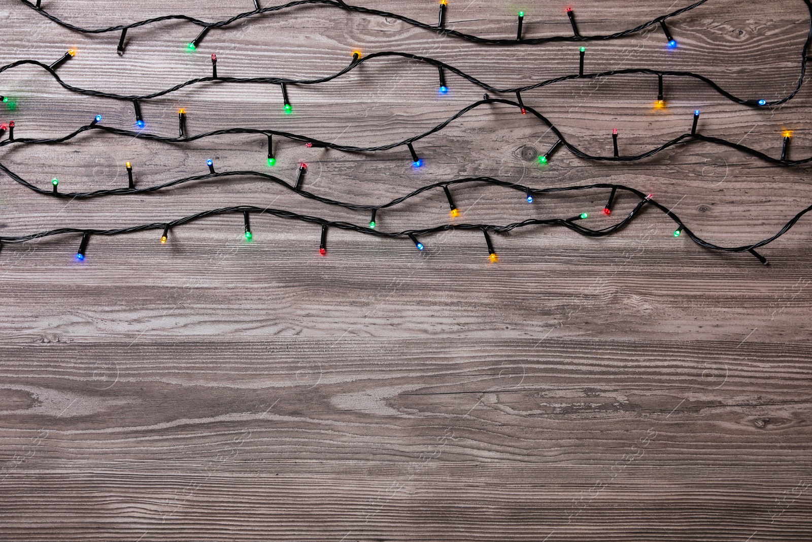 Photo of Christmas lights on wooden table, top view. Space for text