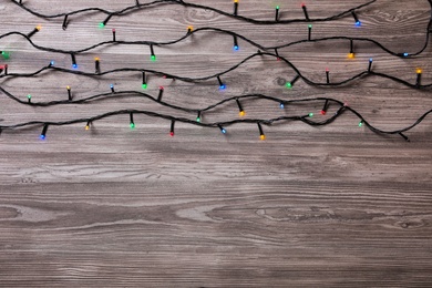 Photo of Christmas lights on wooden table, top view. Space for text