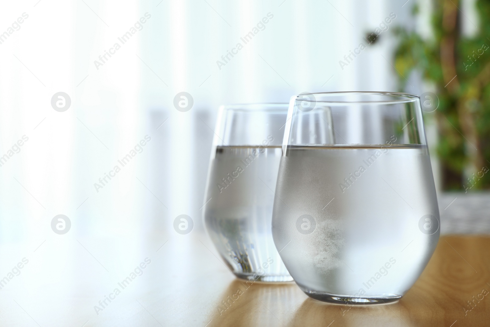 Photo of Glasses full of water on wooden table in room, space for text. Refreshing drink