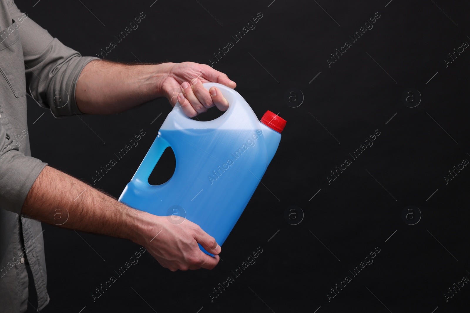 Photo of Man holding canister with blue liquid on black background, closeup. Space for text